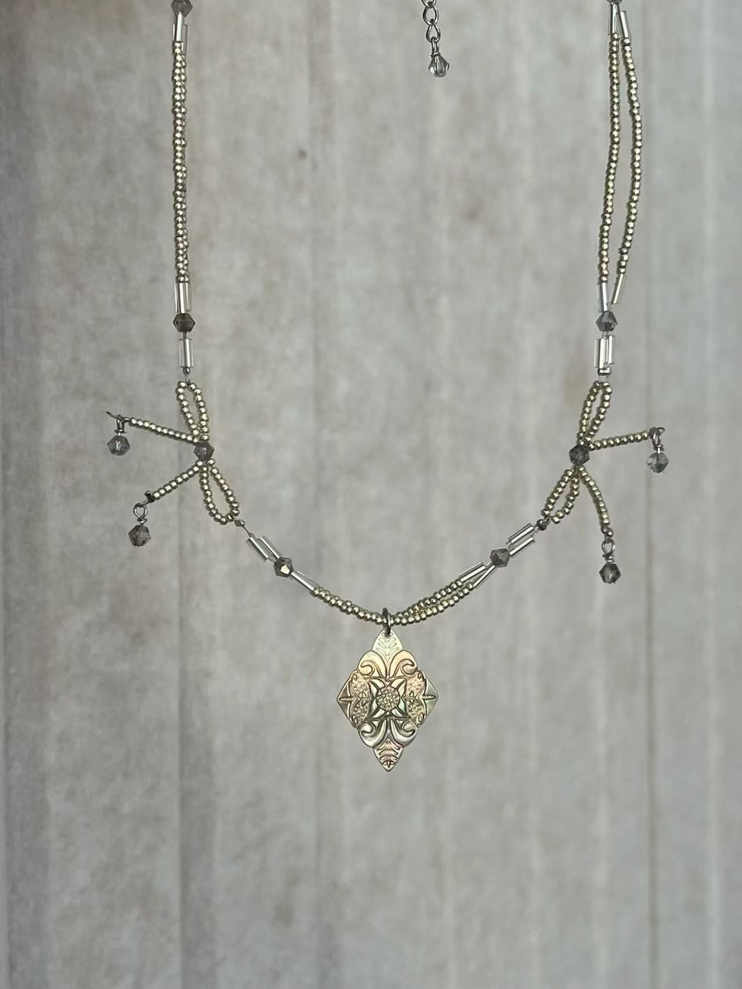 Close-up of engraved silver diamond medallion pendant with handcrafted beaded bows