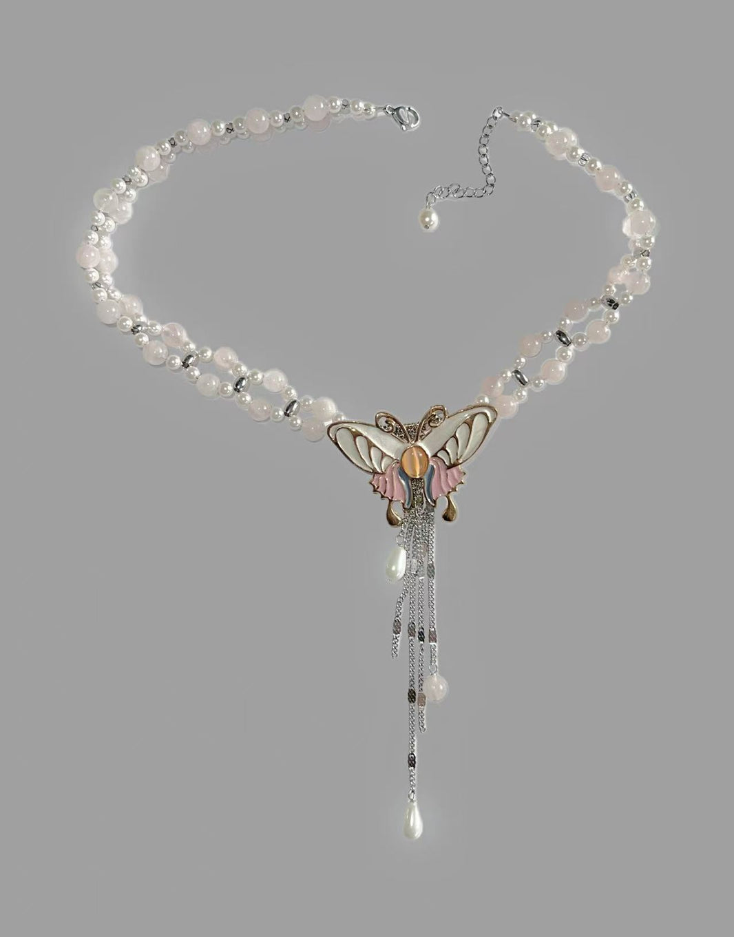 Close-up of enamel pastel pink butterfly pendant with cascading teardrop pearl drops