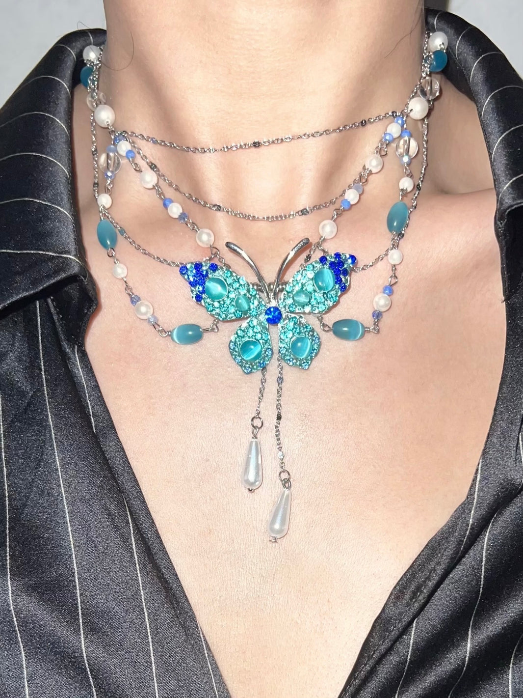 Close-up of rhinestone blue butterfly pendant with dangling tear drop pearl
